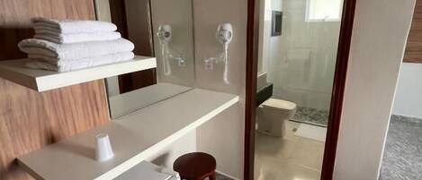 Une salle de bain moderne avec un meuble-lavabo, un miroir, un porte-serviettes, un petit tabouret et un espace douche visible à travers une porte en verre.