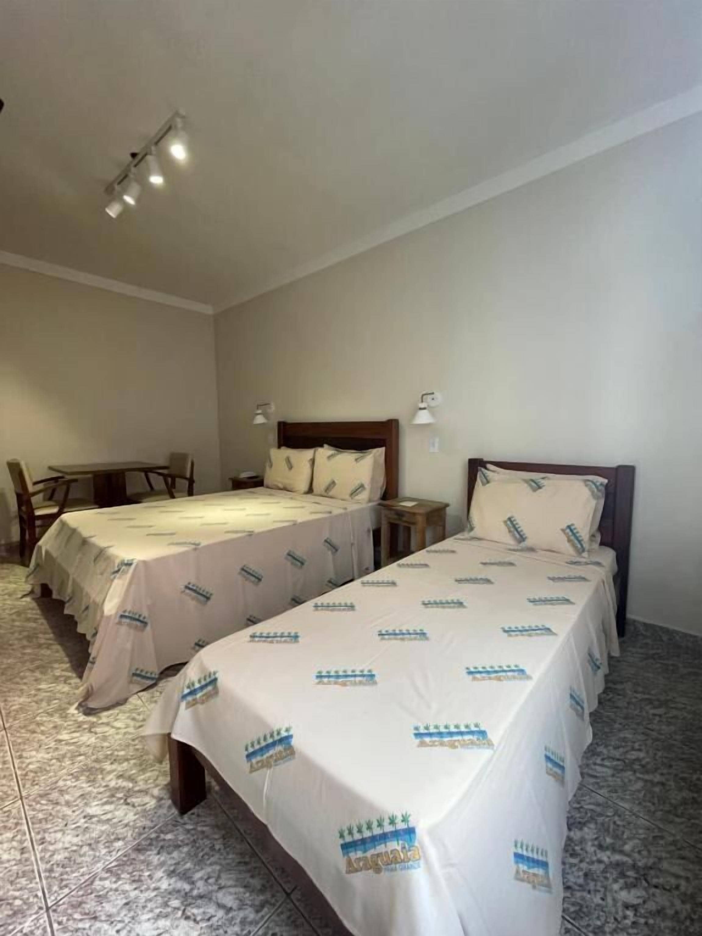 Quarto de hotel com duas camas, uma mesinha e uma mesa de cabeceira.