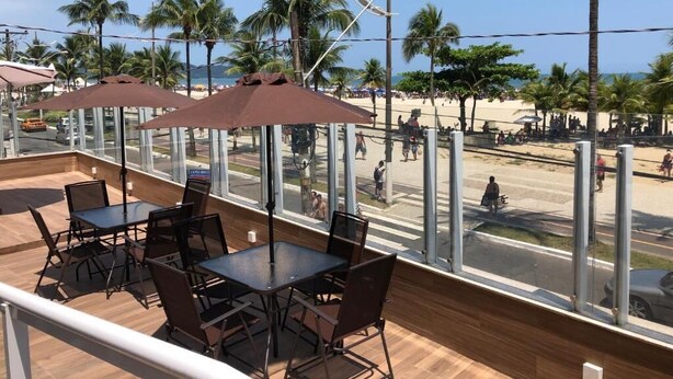 An outdoor seating area with tables and chairs, overlooking a beach with palm trees and a clear sky. - Hotel Araguaia (Praia Grande)
