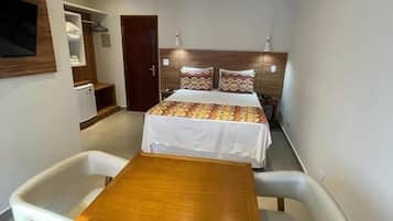 A compact hotel room with a bed, a wooden table, and two white chairs.