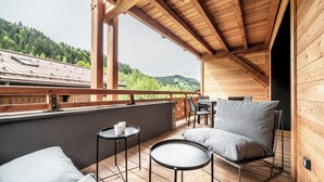 Eine Holzterrasse mit Tisch und Stühlen, einer Sitzecke und Blick auf einen bewaldeten Hang.
