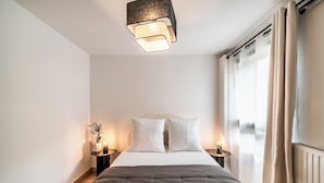 Ein Schlafzimmer mit Bett, Nachttischen, einer Lampe und einem Fenster mit Vorhängen.