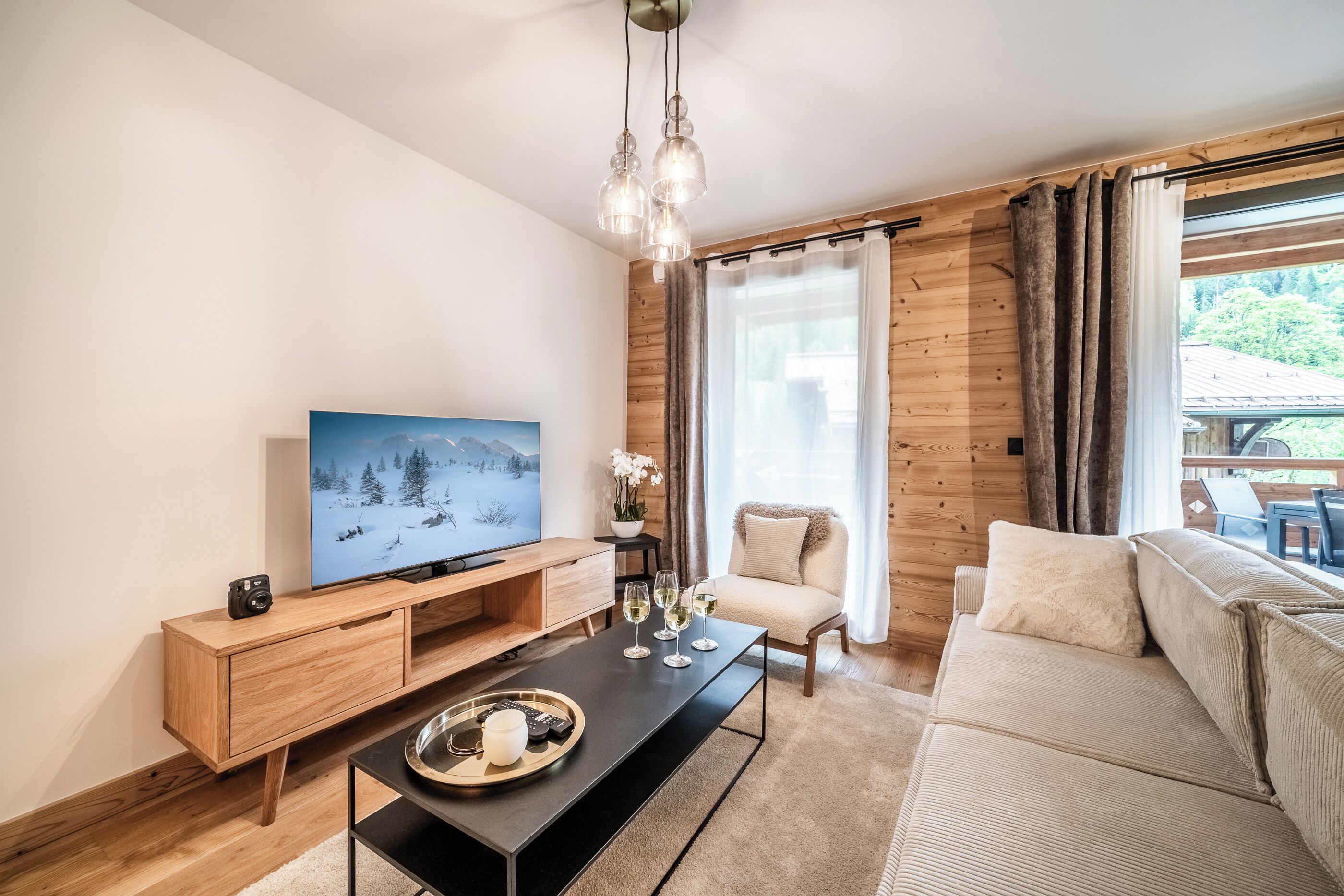 A modern living room with a wooden floor, a flat-screen TV, a black coffee table, a beige sofa, and a wooden cabinet.