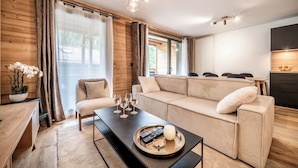 Ein modernes Wohnzimmer mit einem beigen Sofa, einem Couchtisch mit Fernbedienungen und Gläsern sowie einer Wand mit Holzverkleidung.