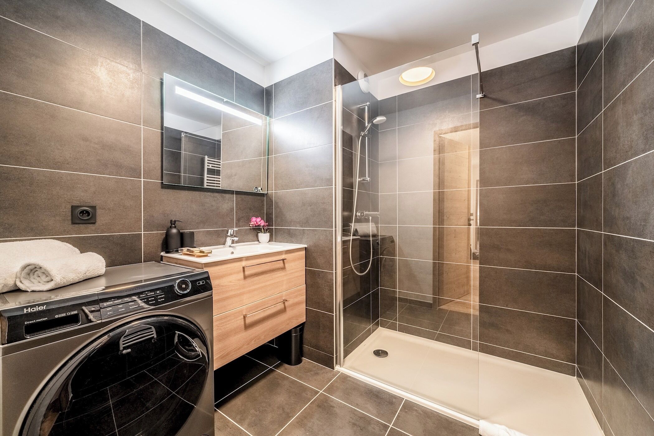 A modern bathroom with a washing machine, a vanity with a mirror, and a walk-in shower.