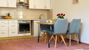 Una cocina compacta con armarios blancos, horno integrado y comedor con dos sillas y una mesa.