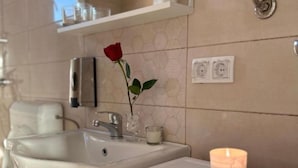 Un baño con un lavabo blanco, una rosa en un florero de vidrio, una vela y una pequeña bandeja decorativa con piedras.