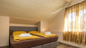 Une chambre avec un plafond en pente, un lit avec deux oreillers, une table de chevet et une fenêtre avec des rideaux.