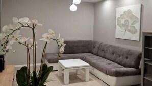 A modern living room with a grey sectional sofa, a white coffee table, and white orchids. - Pansion Belvedere - One Bedroom (Magnolia) (Mali Losinj)