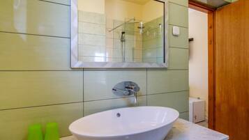 A bathroom with a white sink, a mirror, and a shower. There are two green bottles on the counter.