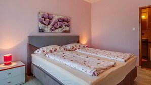 A double bed with floral bedding, a bedside table with a red lamp, and a painting of flowers on the wall.