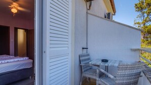 A small balcony with a table and two chairs, a bed inside the room, and a ceiling fan.