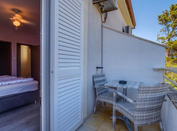 A small balcony with a table and two chairs, a bed inside the room, and a ceiling fan.