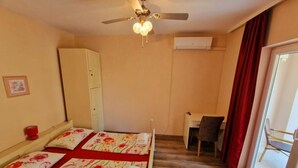 Un dormitorio con dos camas, un escritorio, una silla, un ventilador de techo y una ventana con cortinas.