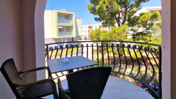 Un balcón con mesa y sillas, con vistas a un jardín con árboles y un edificio al fondo.