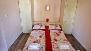 Una habitación con dos camas, un corredor rojo para la cama y cabeceras blancas. Hay dos aparadores blancos y un objeto pequeño rojo en la mesita de noche.