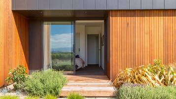 Een modern gebouw met een houten gevel, een glazen entree en een pad dat leidt naar een slaapkamer met een bed en uitzicht op de omgeving.