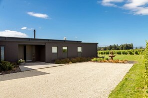 A modern building with a gravel driveway, a water feature, and a vineyard in the background.