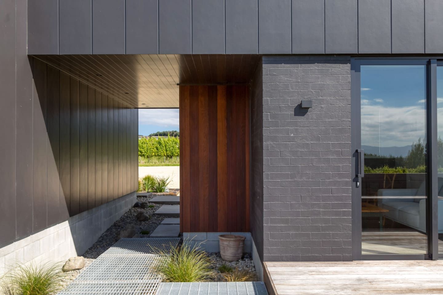 A modern building with a dark facade, a wooden door, and a glass entrance.