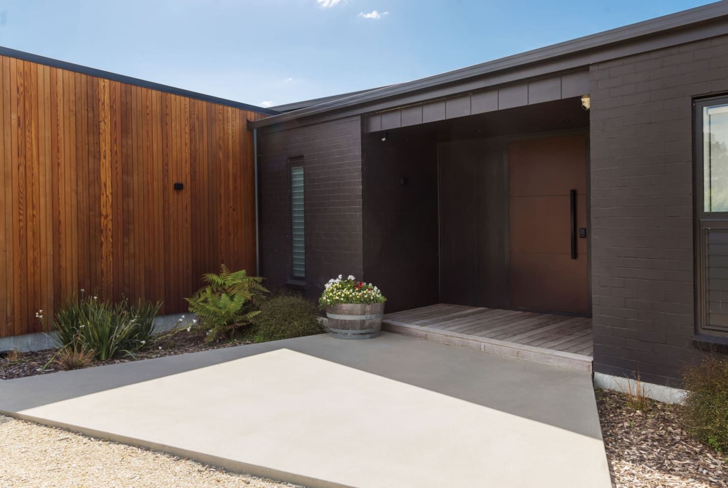 A modern house with a wooden exterior, a concrete patio, and a small garden with plants and flowers.