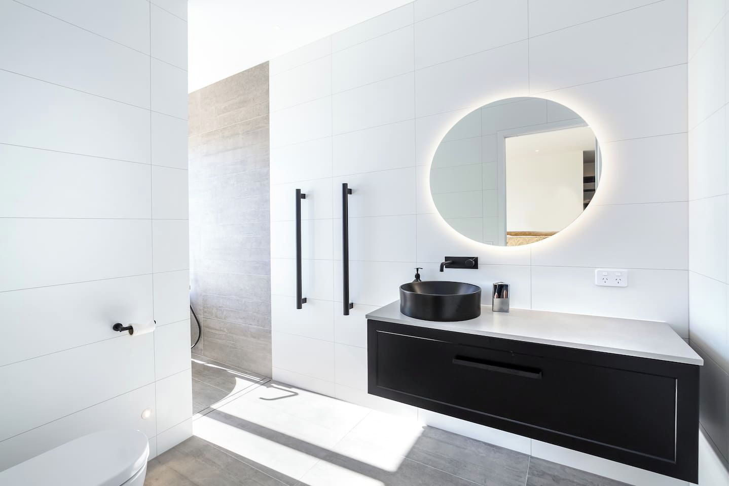 Une salle de bain moderne avec un grand miroir, un meuble-lavabo noir et blanc et un luminaire circulaire.
