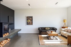 A modern living room with a fireplace, a sofa, a coffee table, and a rug. - 89 In The Vines, Martinborough (Martinborough)