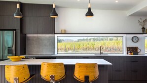 Une cuisine moderne dotée d’une grande fenêtre, de meubles de rangement aux couleurs sombres et de trois tabourets de bar en bois.