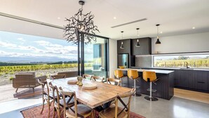 A modern kitchen with a large island, bar stools, and a view of vineyards. - 89 In The Vines, Martinborough (Martinborough)