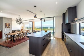 A modern kitchen with a central island, dark cabinetry, and pendant lighting. - 89 In The Vines, Martinborough (Martinborough)