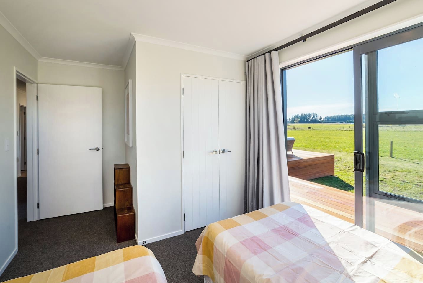 A hotel room with two beds, a wardrobe, a small wooden cabinet, and a large sliding glass door leading to an outdoor deck.