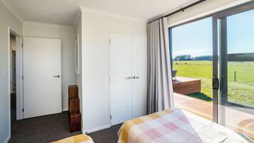 A hotel room with two beds, a wardrobe, a small wooden cabinet, and a large sliding glass door leading to an outdoor deck.