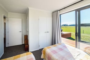A hotel room with two beds, a wardrobe, a small wooden cabinet, and a large sliding glass door leading to an outdoor deck.