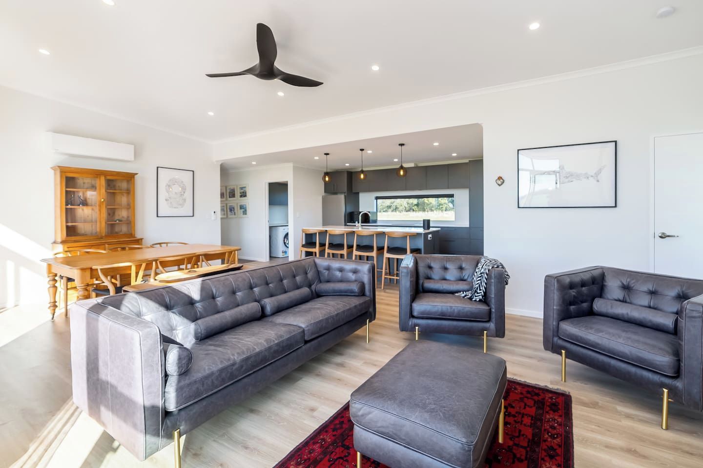 A modern living room with a sectional sofa, two armchairs, and a red patterned rug.