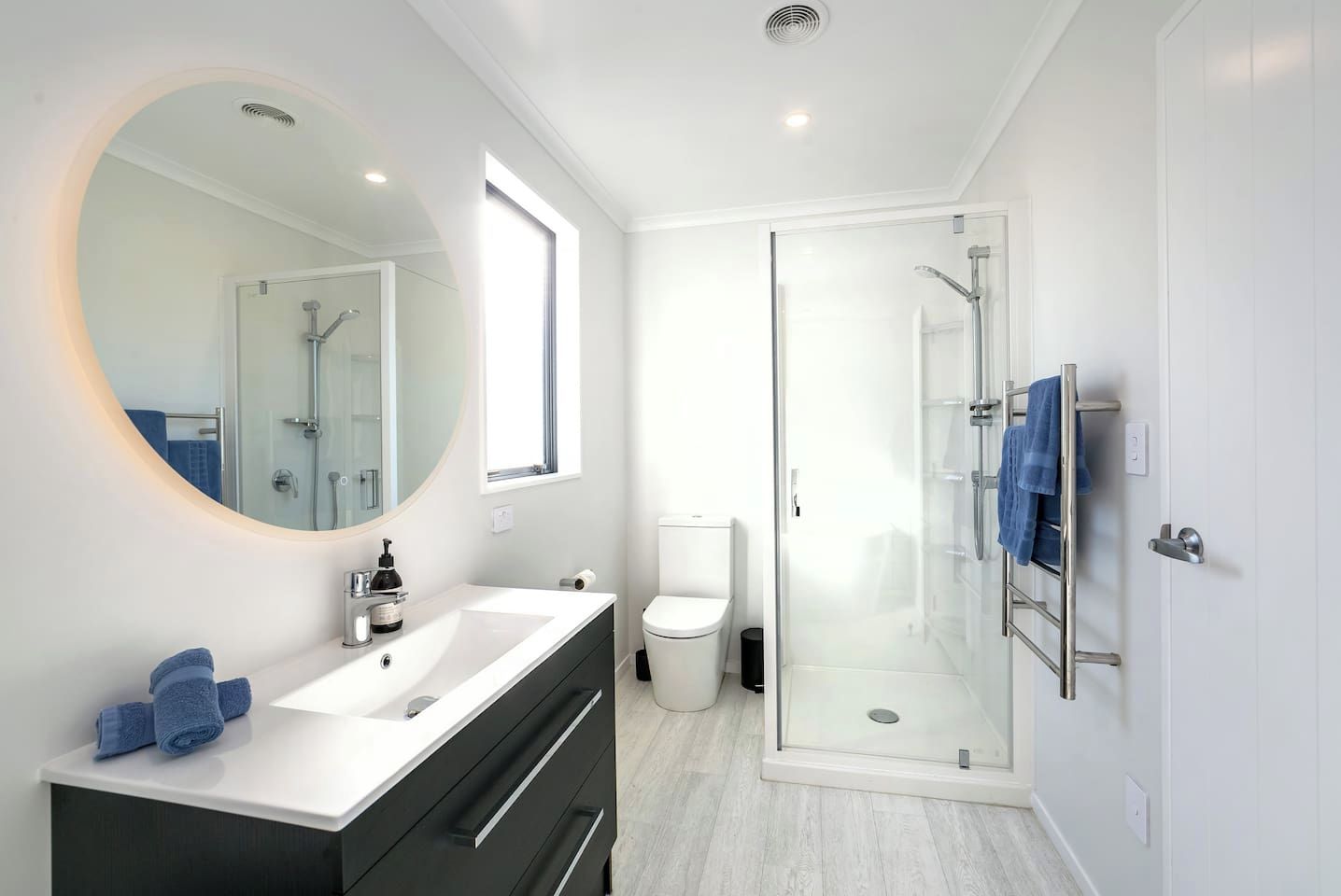 A modern bathroom with a glass-enclosed shower, a round mirror, a white sink, and a black vanity.