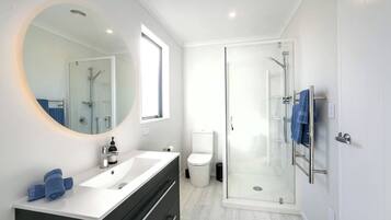 A modern bathroom with a glass-enclosed shower, a round mirror, a white sink, and a black vanity.