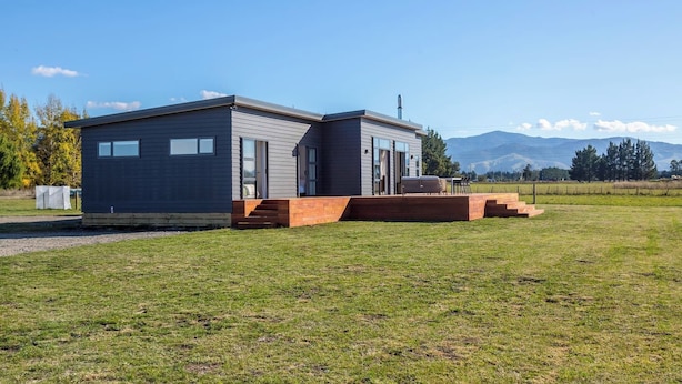 Una casa moderna de dos pisos con techo plano, ventanas amplias y una terraza de madera.