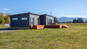 Una casa moderna de dos pisos con techo plano, ventanas amplias y terraza de madera.