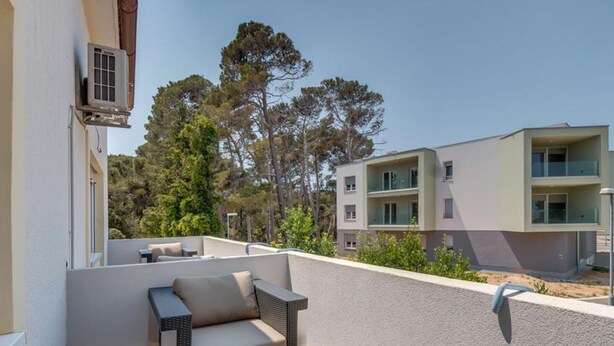 A balcony with outdoor furniture, including a sofa and a table, overlooking a residential area with trees and modern buildings.