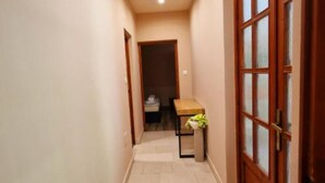 A narrow hallway with a wooden door on the right and a bench in the center.