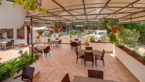 Eine Terrassengaststätte mit Tischen und Stühlen, umgeben von hängenden Blumenkästen und Topfpflanzen.