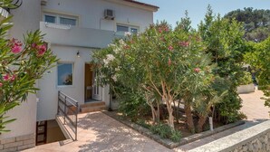 Ein zweistöckiges Gebäude mit Balkon, Steinmauer und Garten mit blühenden Pflanzen.