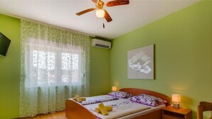 Ein Schlafzimmer mit einem hölzernen Bett, grünen Wänden, einem Deckenventilator, einem Fenster mit durchsichtigen Vorhängen und einer wandmontierten Klimaanlage.