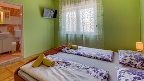 Ein Zimmer mit zwei Betten, einem an der Wand befestigten Fernseher und einem durch eine offene Tür einsehbaren Badezimmer.