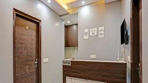 A reception area with a marble counter, wooden door, and a ceiling fan. - Hotel Heven (New Delhi)