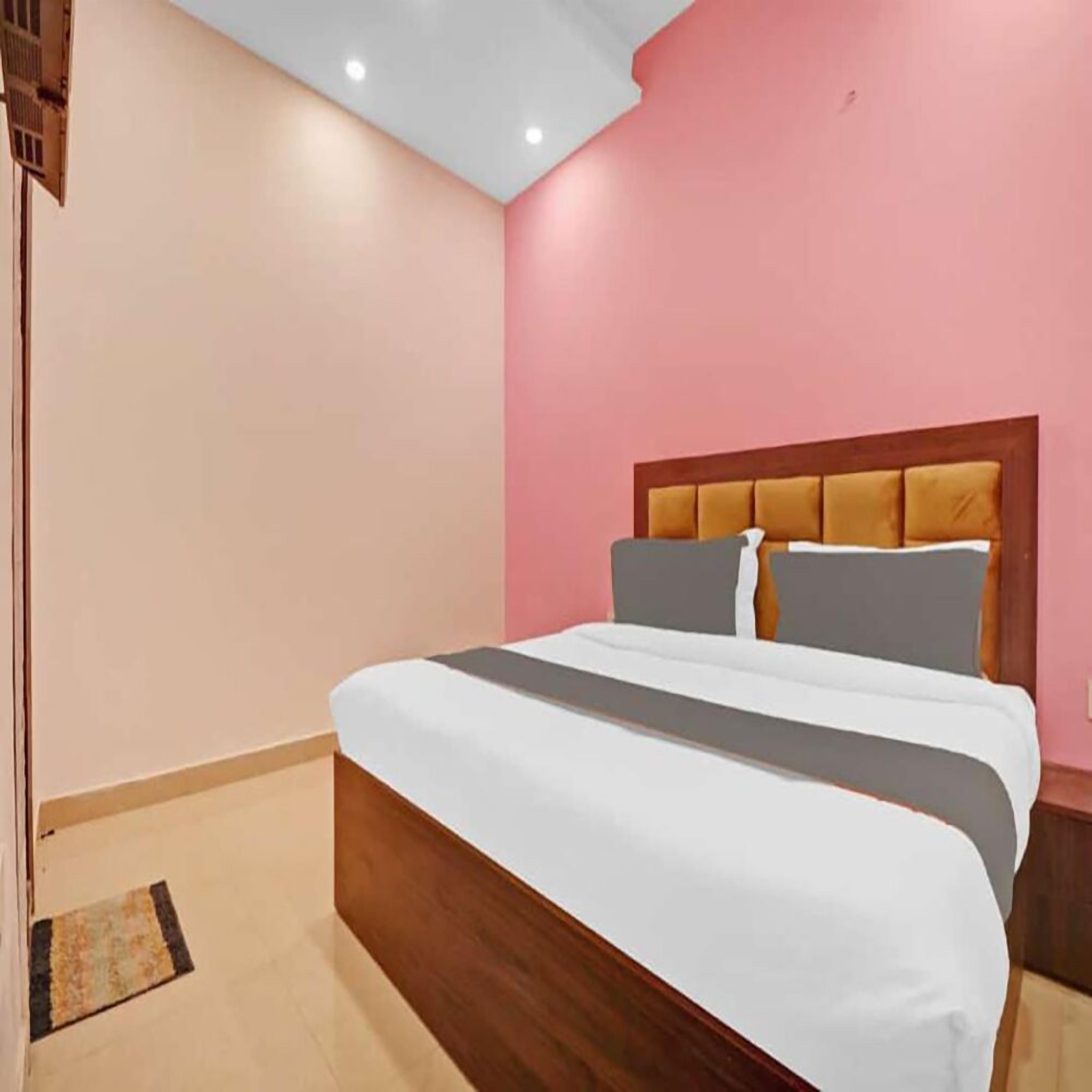 A bedroom with a wooden bed frame, a pink wall, and a ceiling with recessed lighting.
