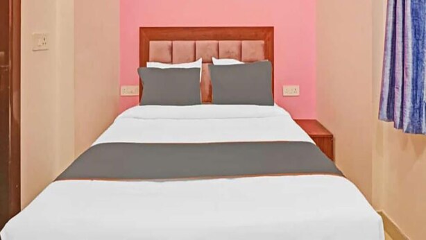 A bedroom with a wooden headboard, a bed with white and gray bedding, and a pink wall. - Hotel Heven (New Delhi)