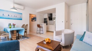Ein modernes Wohnzimmer mit einer Couch, einem Holztisch und einem Essbereich mit Tisch und Stühlen. Im Hintergrund ist eine Küche erkennbar.