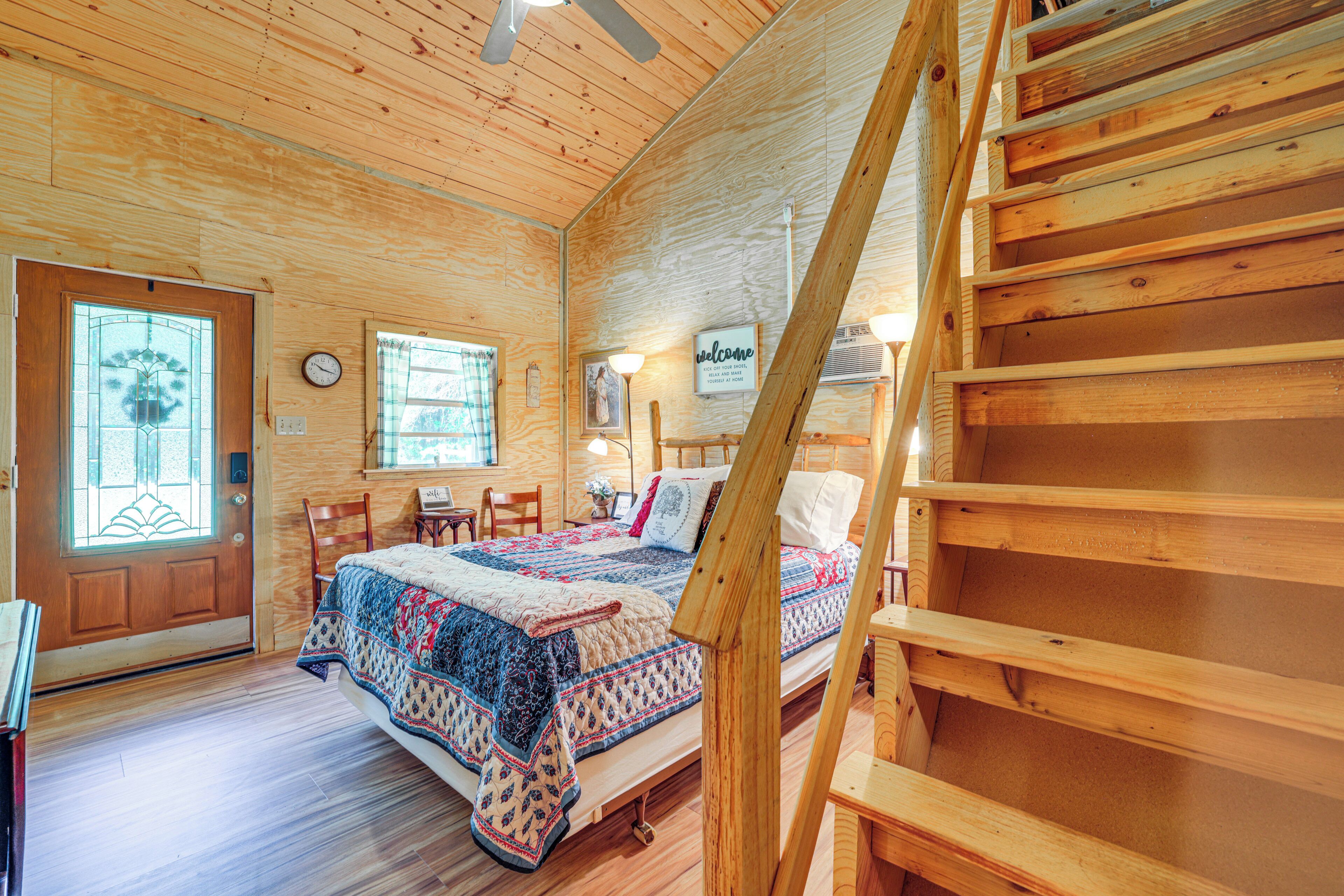 Ein Interieur einer Holzhütte mit einem Bett, einer Treppe und einer Tür mit einem Buntglasfenster.
