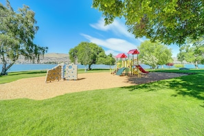 Un parque infantil con estructuras para escalar y toboganes, rodeado de árboles y un lago.