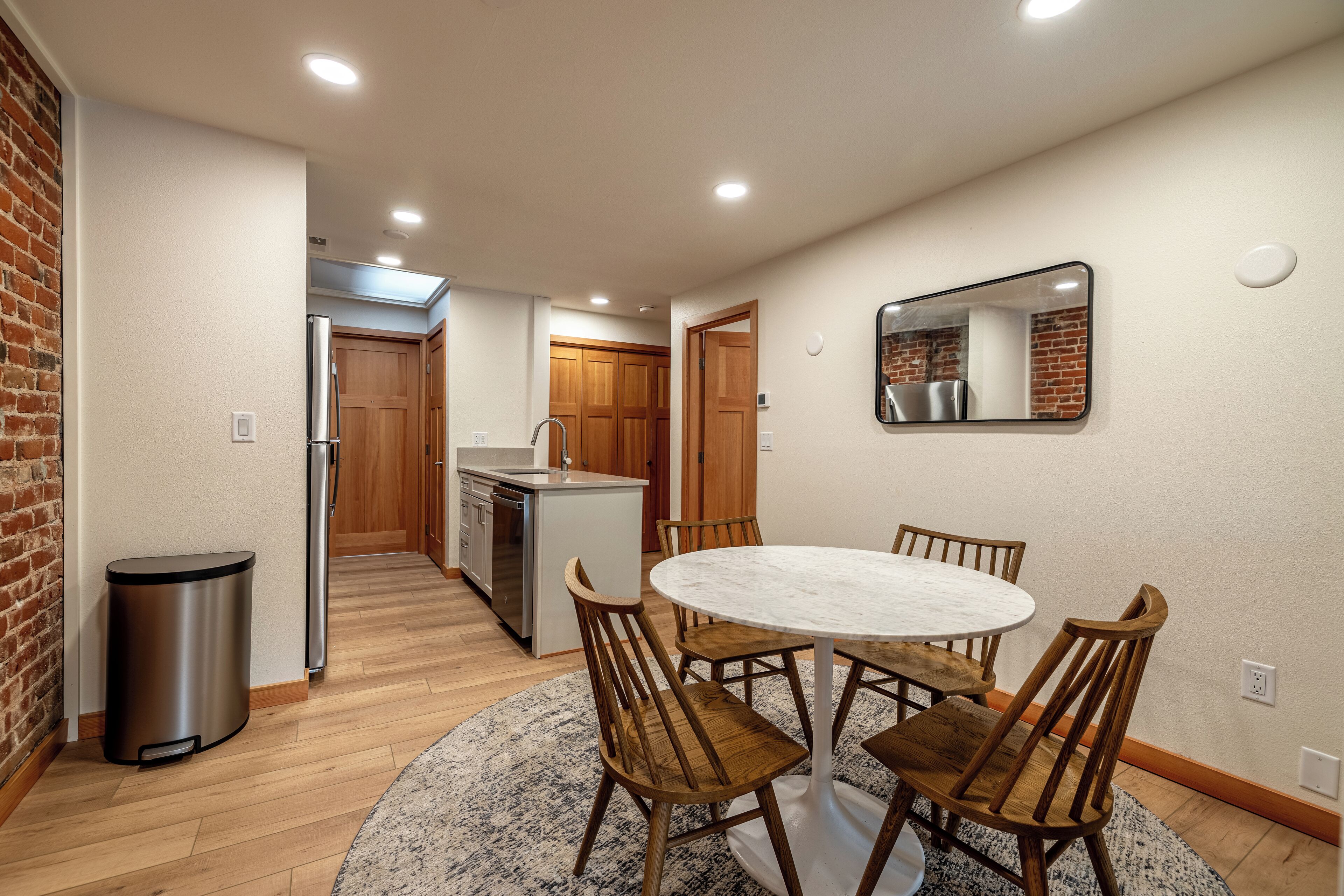 A modern kitchen with wooden cabinets, a stainless steel refrigerator, and a dining area with a round table and wooden chairs.